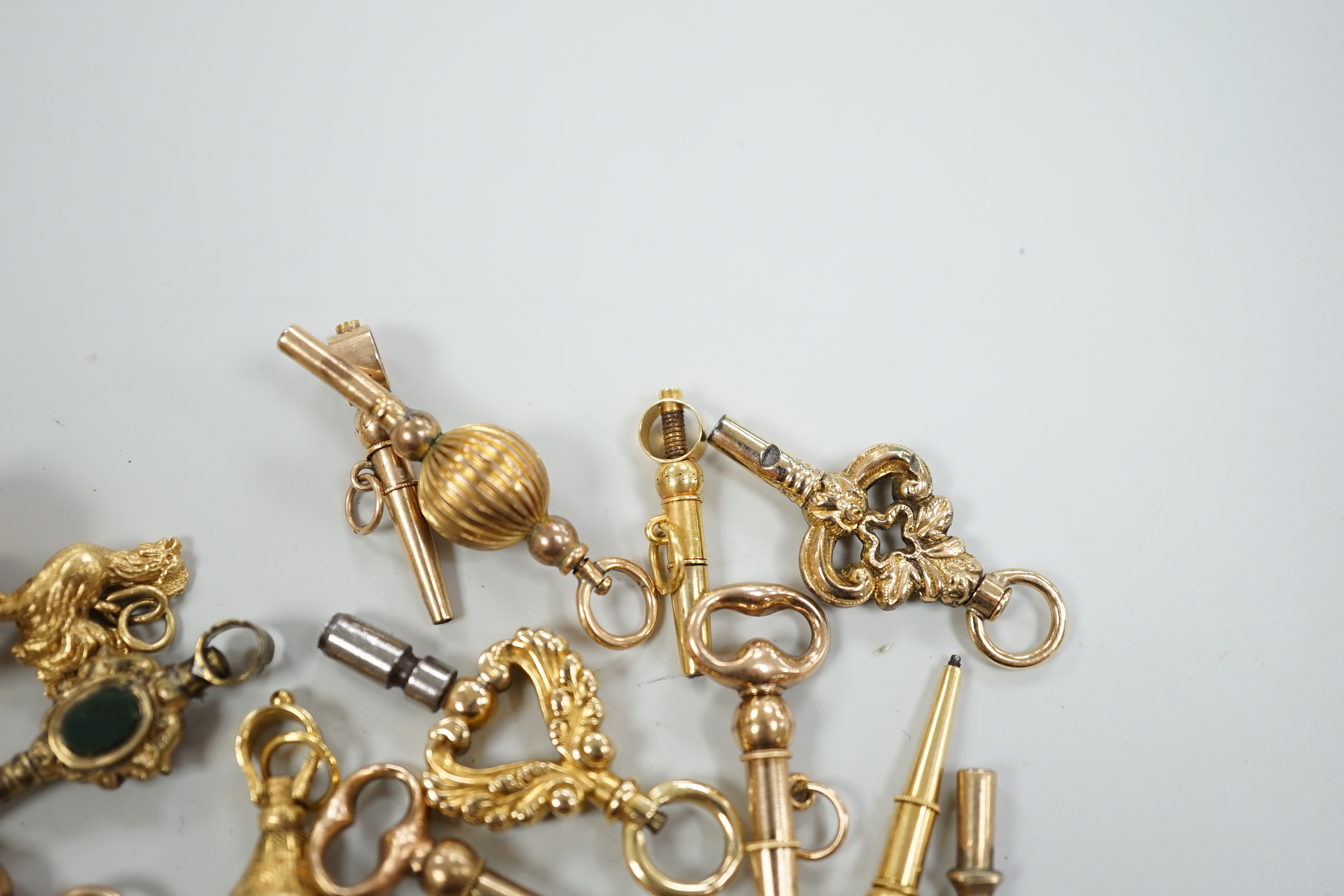 Twenty assorted mainly 19th century yellow metal small watch keys, including trade insignia, bloodstone set and keys to be turned in one direction, largest 37mm, together with a 19th century yellow metal overlaid and aga